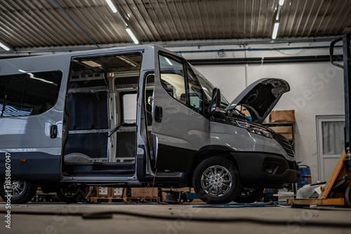 Commercial vans in industrial workshop during conversion and assembly. Vehicle interiors exposed, doors open, showing custom transport production, maintenance, and manufacturing process.