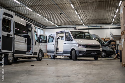 Commercial vans in industrial workshop during conversion and assembly. Vehicle interiors exposed, doors open, showing custom transport production, maintenance, and manufacturing process.