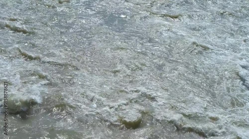 Raging river water flowing rapidly downstream. Powerful white water rapids surging downstream, revealing raw natural energy through turbulent, foaming currents cascading across rugged river landscape