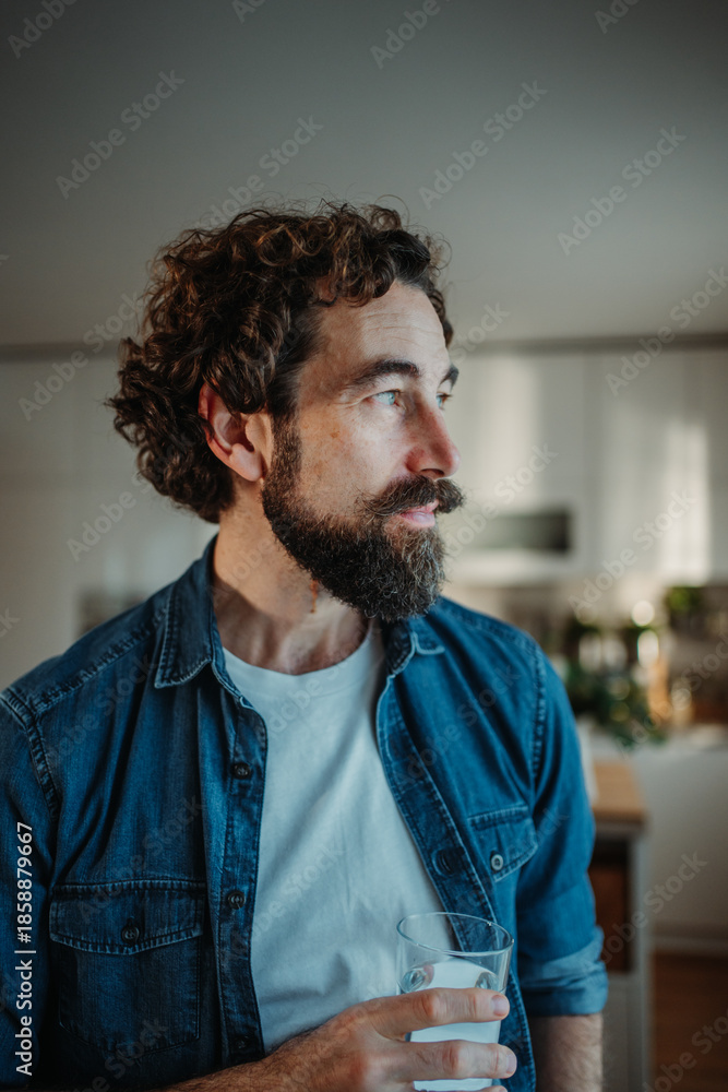 Obraz premium Man drinking water in kitchen contemplating morning health