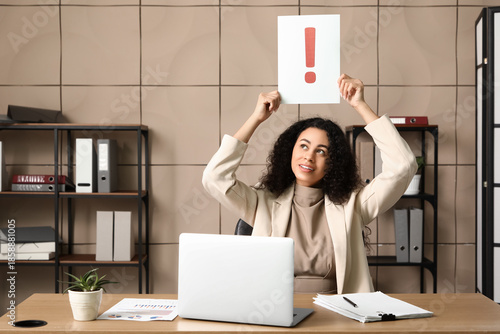 Foto Happy young African-American businesswoman with laptop holding paper sheet of ex
