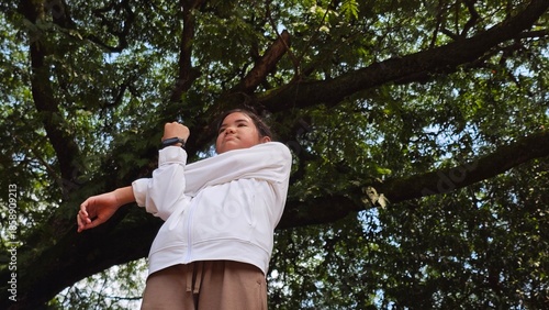 South East Asian girl doing stretch exercisefor warming up before running or jogging in the park. The girl wearinglong white sleeve sport attire and black smart band.