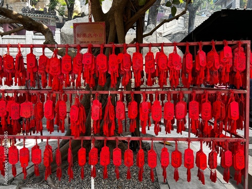 Red wishing tags or prayer cards, known as fai chun or wish cards, hanging in rows on a red metal rack at a Chinese temple