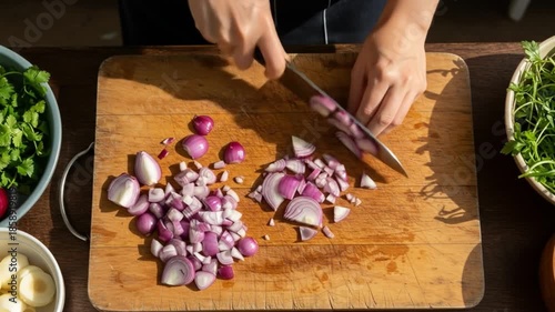 A person chopping red onions on a wooden cutting board with a knife, surrounded by bowls of greens and garlic. Perfect for cooking, recipes, food blogs.