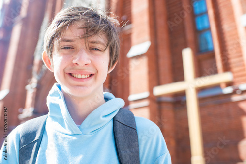Slika na platnu Portrait of a smiling 13 year old boy with a backpack in front of a Catholic church