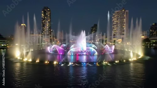 A colorful, illuminated water fountain display at night with city lights