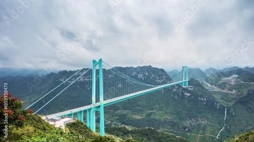 Wallpaper Mural time-lapse of the Huajiang Canyon Bridge in Guizhou, China, under cloudy skies. A stunning suspension bridge spans a deep mountain canyon with lush green peaks. Torontodigital.ca