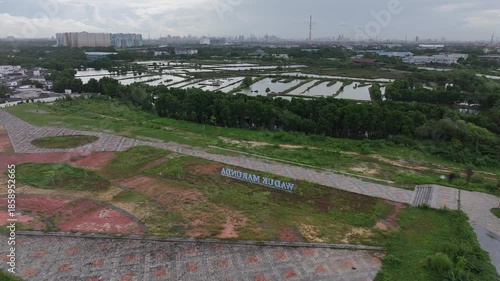 Aerial view of city streets, green trees, a lake, and tall buildings, under a clear blue sky.waduk marunda jakarta