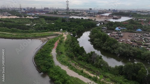 Aerial view of city streets, green trees, a lake, and tall buildings, under a clear blue sky.waduk marunda jakarta