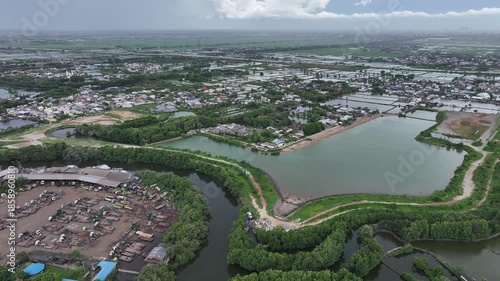 Aerial view of city streets, green trees, a lake, and tall buildings, under a clear blue sky.waduk marunda jakarta