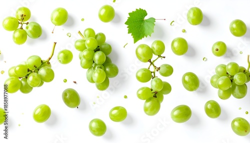 Overhead view of scattered green grapes, stems, and a single leaf on a white backdrop