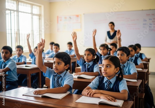 Indian school children raising hands while sitting at desks in a classroom during lesson. Primary education and learning process concept.