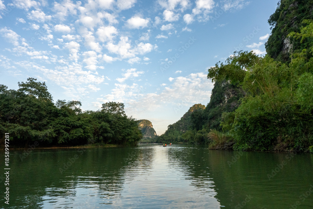Obraz premium Peaceful River With Distant Rowing Boats and Karst Mountains in Trang An, Ninh Binh, Vietnam