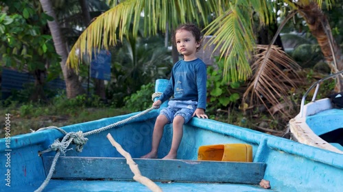 curious child pointing while sitting in small boat near tropical beach