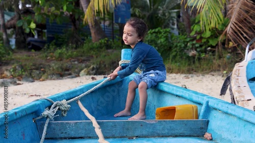 toddler sitting in blue fishing boat and pulling boat rope to navigate