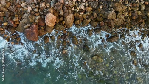Top view shot capturing the beautiful contrast between the deep blue sea foam and the brown textured boulders along the shoreline, creating a natural abstract pattern.concept nature