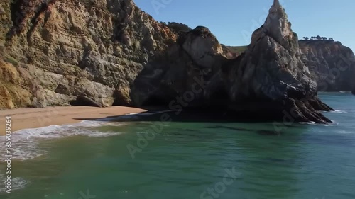 A serene beach scene featuring a sandy shoreline nestled between towering rugged rock formations, with gentle waves lapping at the shore and a clear blue sky