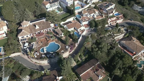 Tilt down aerial of Mijas Pueblo hillside villas with terracotta roofs and pools. Malaga, Andalusia, Spain.