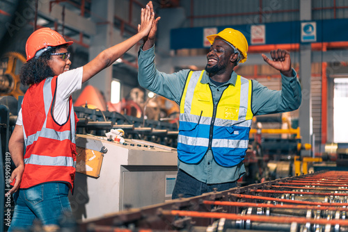 African factory worker man woman shake hand high five success. Industrial engineer partner male female wear safety helmet vest in manufacturing plant. Heavy metal machine background. Happy diversity