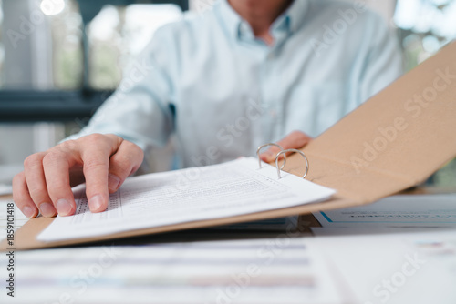 Business professional reviewing documents in a folder at an office desk. Concept of paperwork, administration, contract review, compliance, auditing, and corporate documentation process.