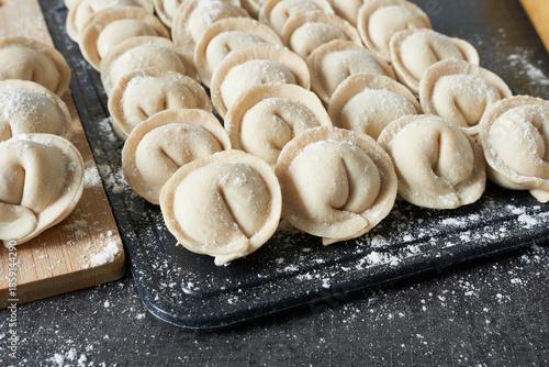 Raw dumplings on a cutting board with flour on a black background