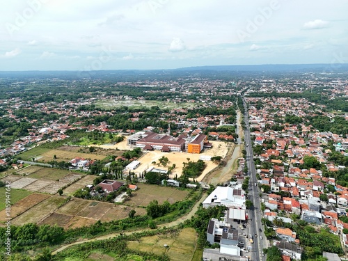 Aerial View of Suburban Residential Area with Green Rice Fields and Main Road in Indonesia