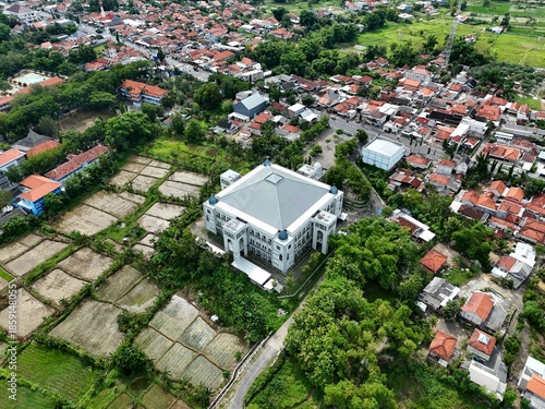 Aerial View of Suburban Village Landscape with Green Rice Fields and Large White Building Under Overcast Sky