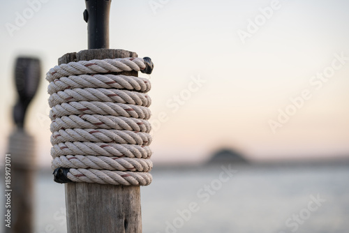 Rope Wrapped Around Wooden Post by Calm Sea at Sunset