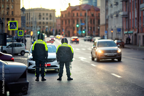 Wallpaper Mural Two police officers in visibility uniforms standing near patrol car, monitoring passing traffic and pedestrians on wide avenue at dusk with historic buildings. Traffic cops on duty, twilight light Torontodigital.ca