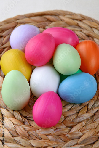 Brightly colored easter eggs, in a natural straw basket against a natural white background.