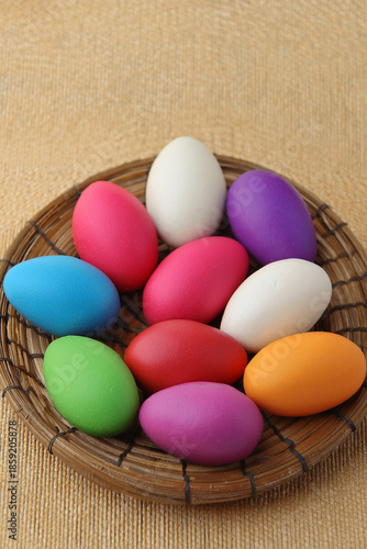 Brightly colored easter eggs, in a straw basket against a natural beige background.
