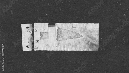 Torn paper strips held together by safety pins on a textured dark background