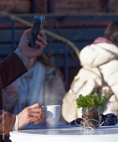 People enjoying hot coffee at a small outdoor table during an advent Naplavka farmers market, with simple winter decoration creating a calm seasonal atmosphere of winter leisure and social meeting.
