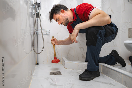 Fotografie Plumber Using Plunger unclogging shower drain in bathroom