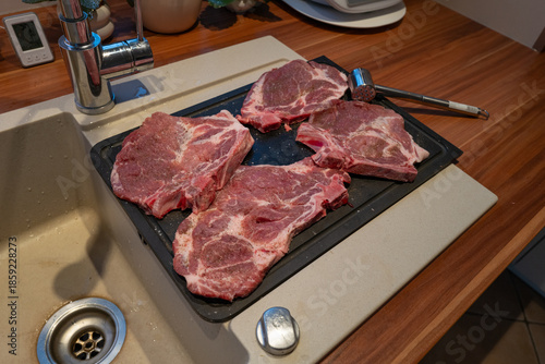 High-quality kitchen scene featuring four raw pork steaks seasoned with salt and pepper, arranged on a black cutting board next to a sink