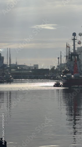 Sailboats and industrial port at Barcelona harbor with calm water reflections