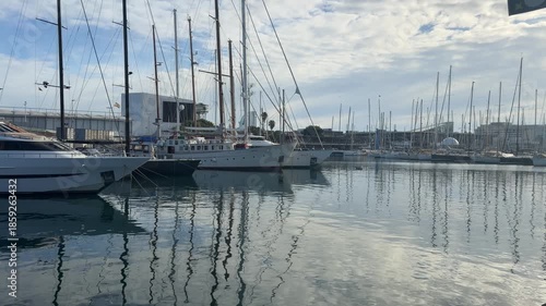 Sailboats and industrial port at Barcelona harbor with calm water reflections