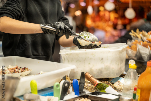 Unrecognizable person wearing gloves scooping cooked octopus into small cups at a market