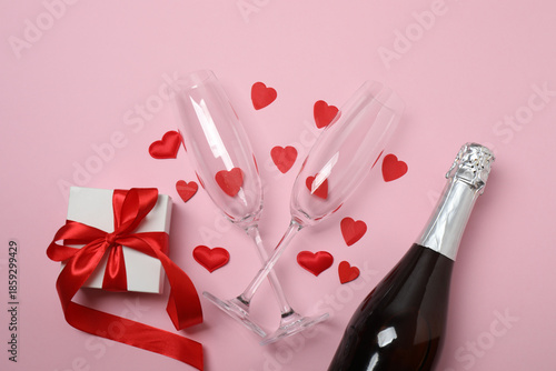 Festive background with a bottle of champagne, two glasses and hearts and gift boxes. A romantic date on Valentine's Day
