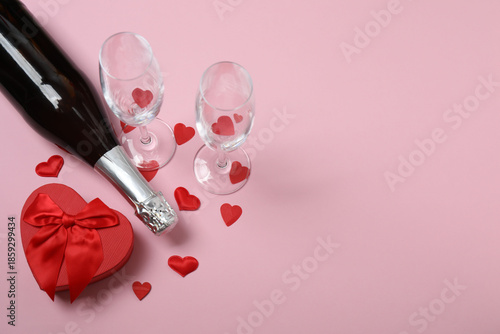 Festive background with a bottle of champagne, two glasses and hearts and gift boxes. A romantic date on Valentine's Day
