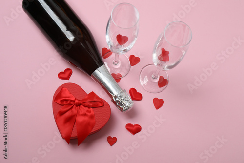 Festive background with a bottle of champagne, two glasses and hearts and gift boxes. A romantic date on Valentine's Day
