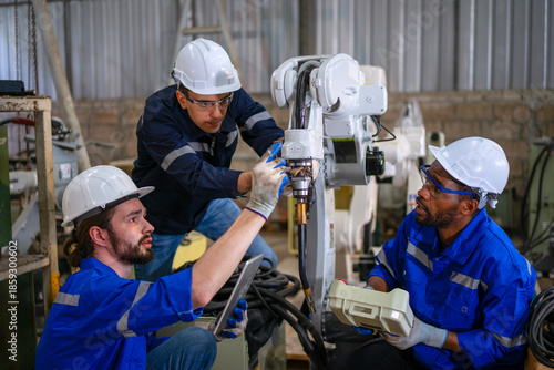 Blue collar workers are working at machine shop with welding robot arm.