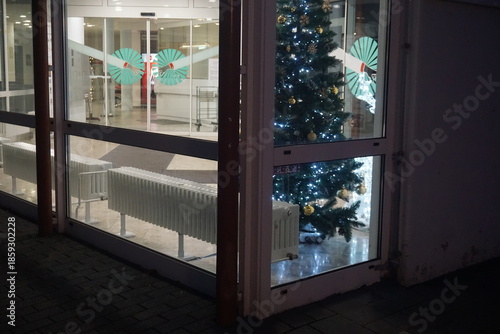Beleuchteter Eingangsbereich von Krankenhaus mit Glasfassaden und geschmückten Christbaum im Innenraum in der Nacht im Winter