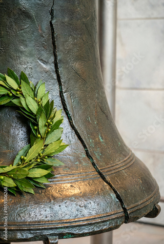 Close up of cracked bronze Liberty Bell with fresh green laurel wreath resting on surface, symbolizing American independence and freedom in historical museum setting