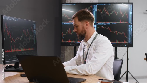 The document is in notepad. Handsome businessman is in the office with stock exchange market information on displays.