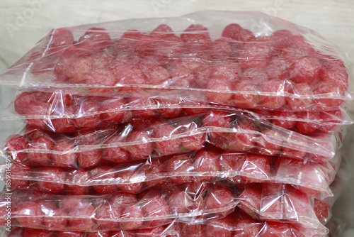 Stacked clear plastic bags of red, round food items, possibly chorizo sausage or dried fruit.

