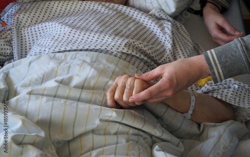 Hand von junger Frau hält Hand von kranker alter Frau im Krankenbett liegend im Krankenhaus 