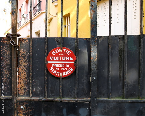 Sortie de voiture. Prière de ne pas stationner.  Panneau rond blanc et rouge d'interdiction de stationner sur une palissade en bois. 