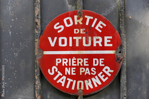 Sortie de voiture. Prière de ne pas stationner.  Panneau rond blanc et rouge d'interdiction de stationner sur une palissade en bois. 