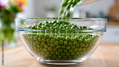 Green Peas Being Poured Into a Glass Bowl on a Wooden Surface